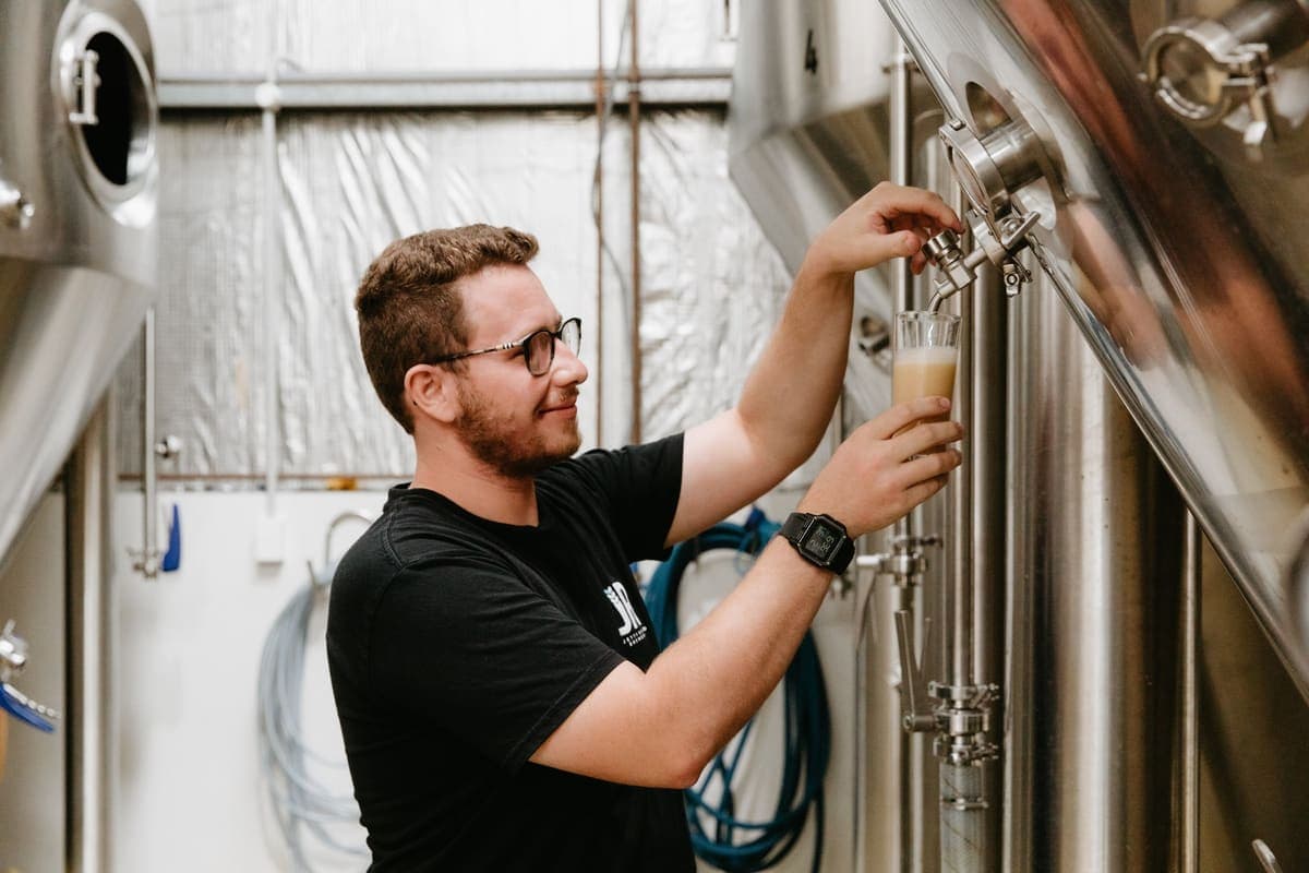 Jetty Road brewer pulling a sample from a stainless fermenter in the brewhouse