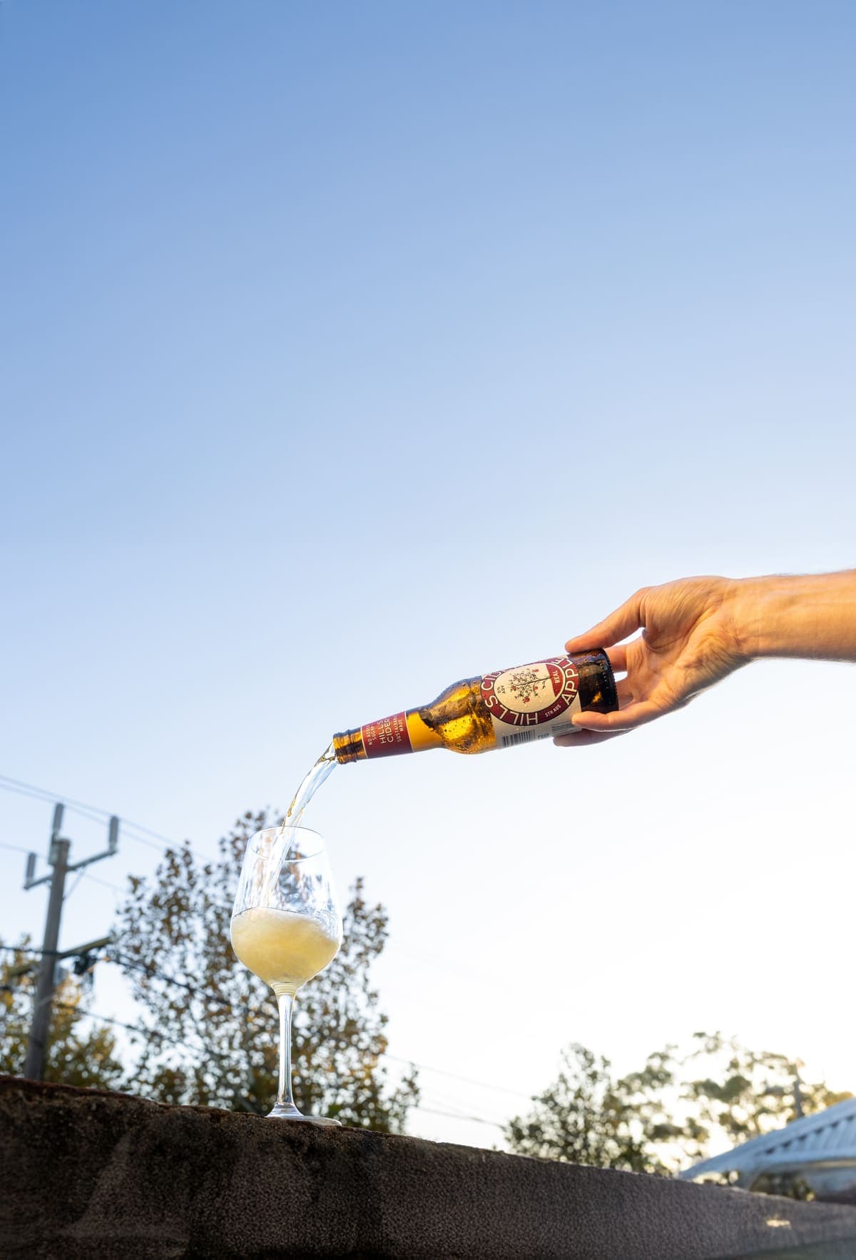 Hills Cider poured into a glass against a blue sky